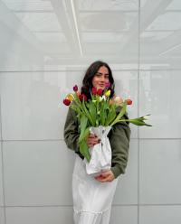 Young woman holding a bouquet of colorful tulips, smiling against a light gray wall.